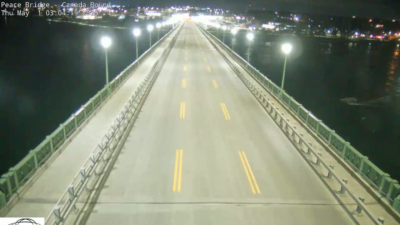 A nearly empty bridge at night, illuminated by streetlights, spans a dark body of water.