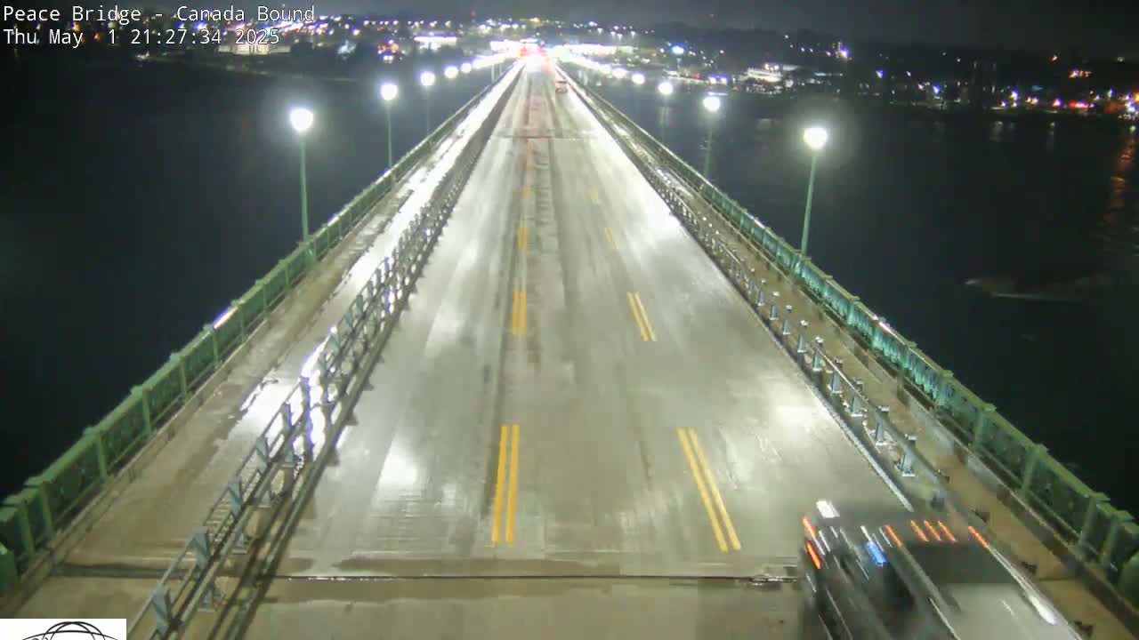 A wet, nighttime view of a bridge with sparse traffic and lights illuminating the roadway and walkways.