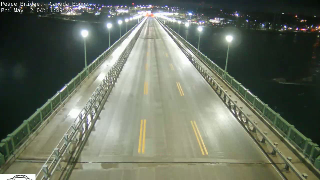 A wet, empty bridge at night is illuminated by streetlights, with dark water visible on either side.