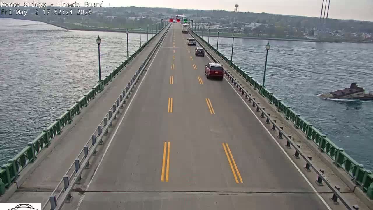 A two-lane bridge over water with several cars driving on it under an overcast sky.