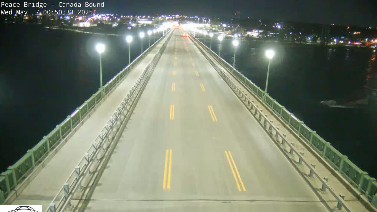 A mostly empty, well-lit bridge at night stretches over dark water, with a few vehicles visible in the distance.