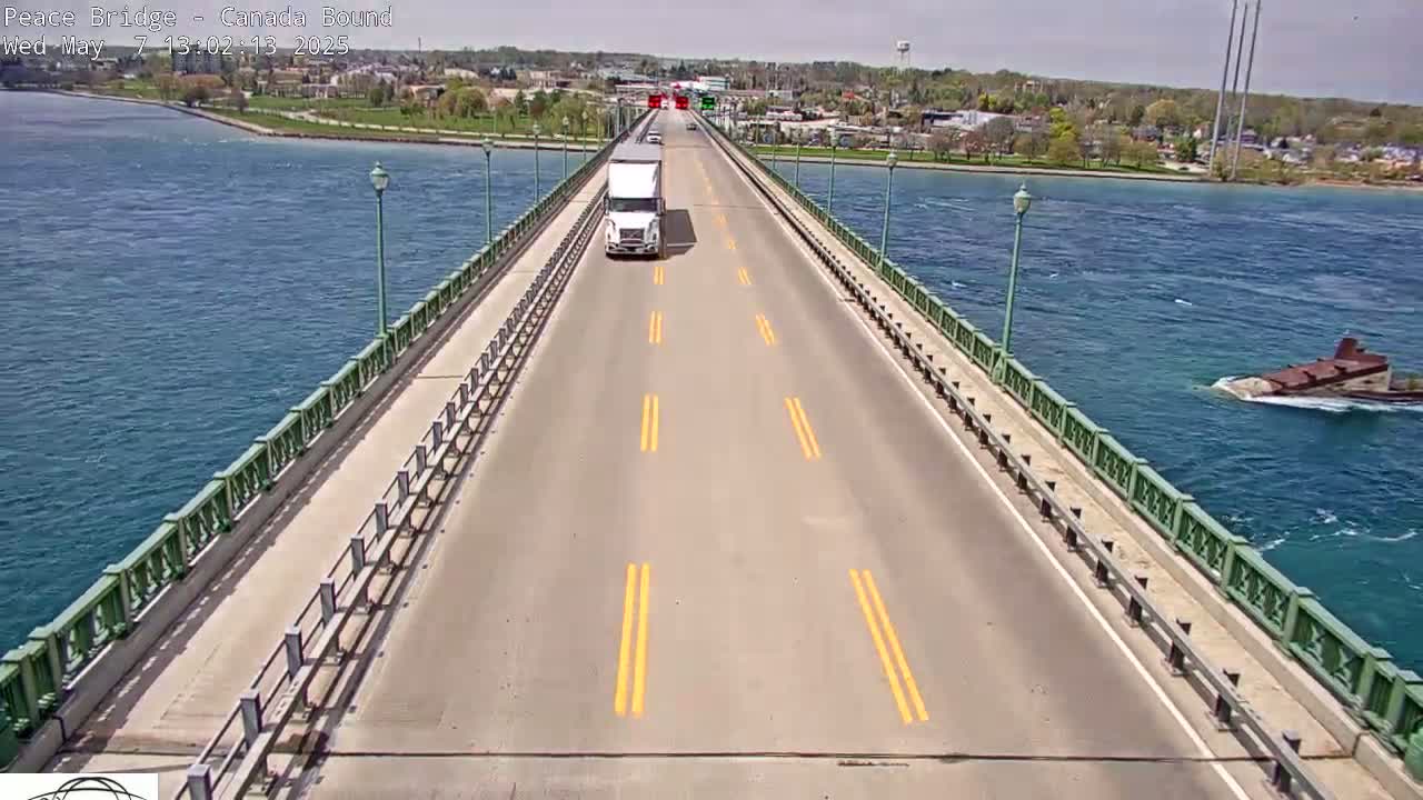 A semi-truck drives across a bridge over a body of water on a sunny day with light chop on the water.