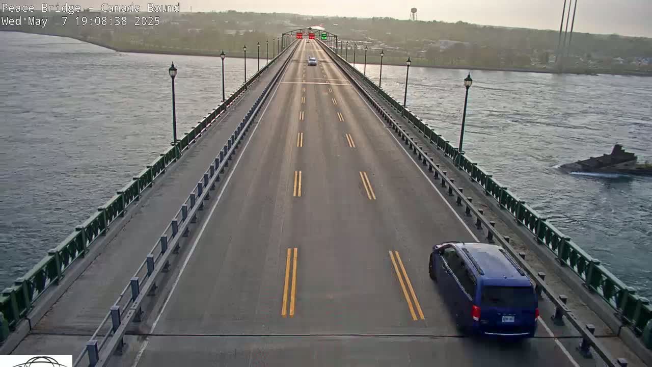 A long bridge spans a body of water under an overcast sky, with a few vehicles traveling on the bridge.