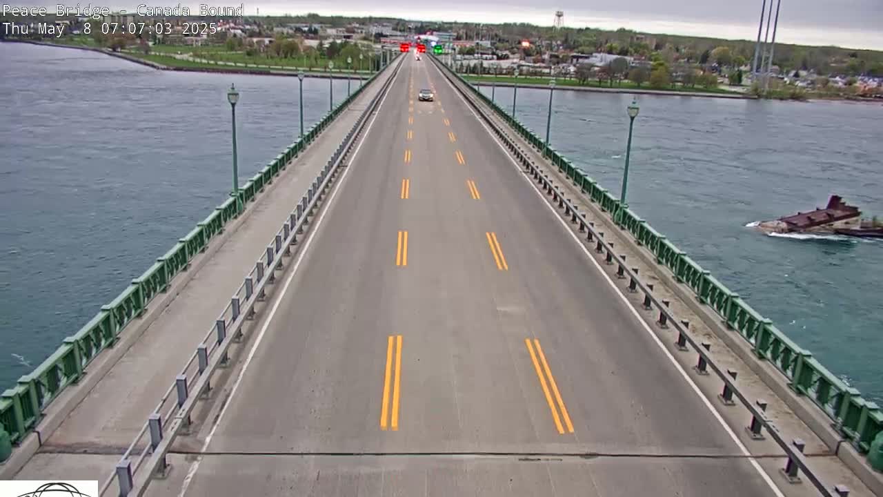 A two-lane bridge over a body of water on an overcast day with a few vehicles visible on the bridge and a barge in the water.