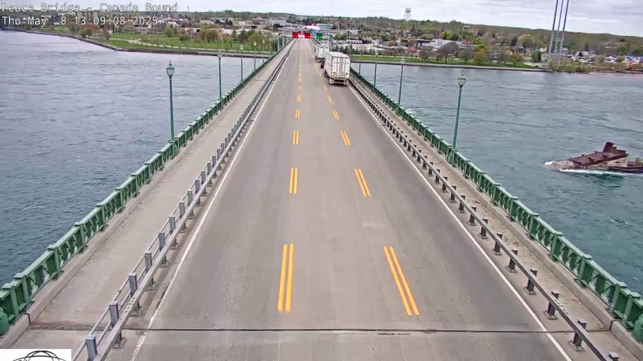 A bridge roadway with a few vehicles on it spans a body of water on a partly sunny day, with a partially submerged ship visible in the water to the right.