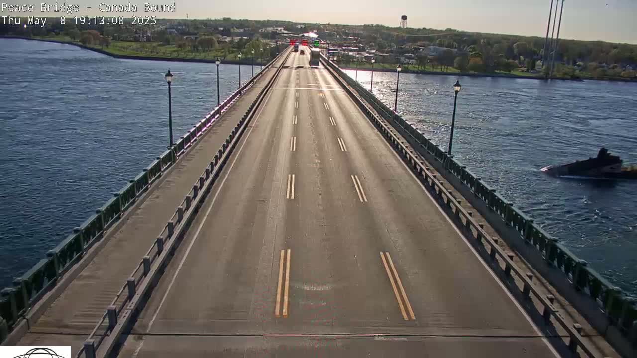A bridge with a few cars driving on it spans a waterway under sunny skies, with a small vessel visible in the water.