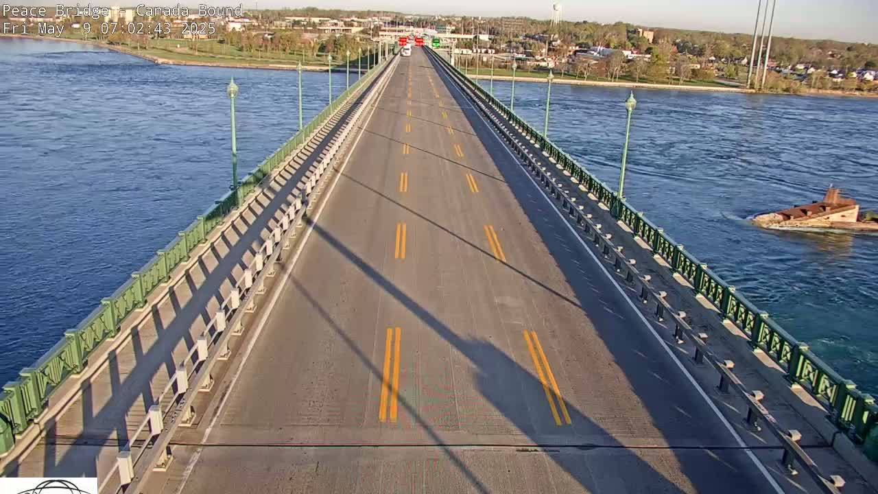 A bridge with a few cars driving on it spans a body of water under sunny conditions.