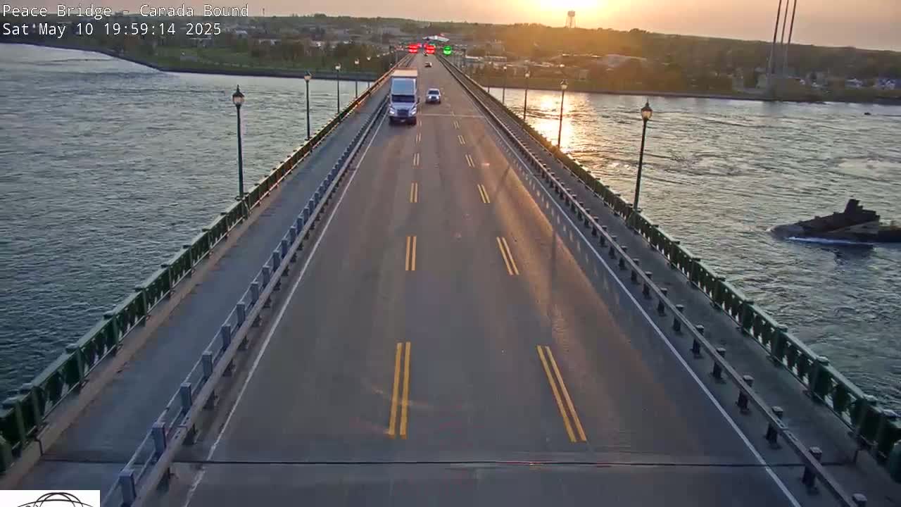 A bridge at sunset with a few vehicles traveling on a multi-lane road, surrounded by calm water.