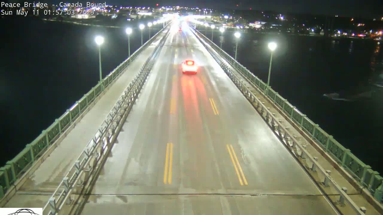 A wet, two-lane bridge at night is lit by streetlights, with a few vehicles driving on it and dark water visible alongside.