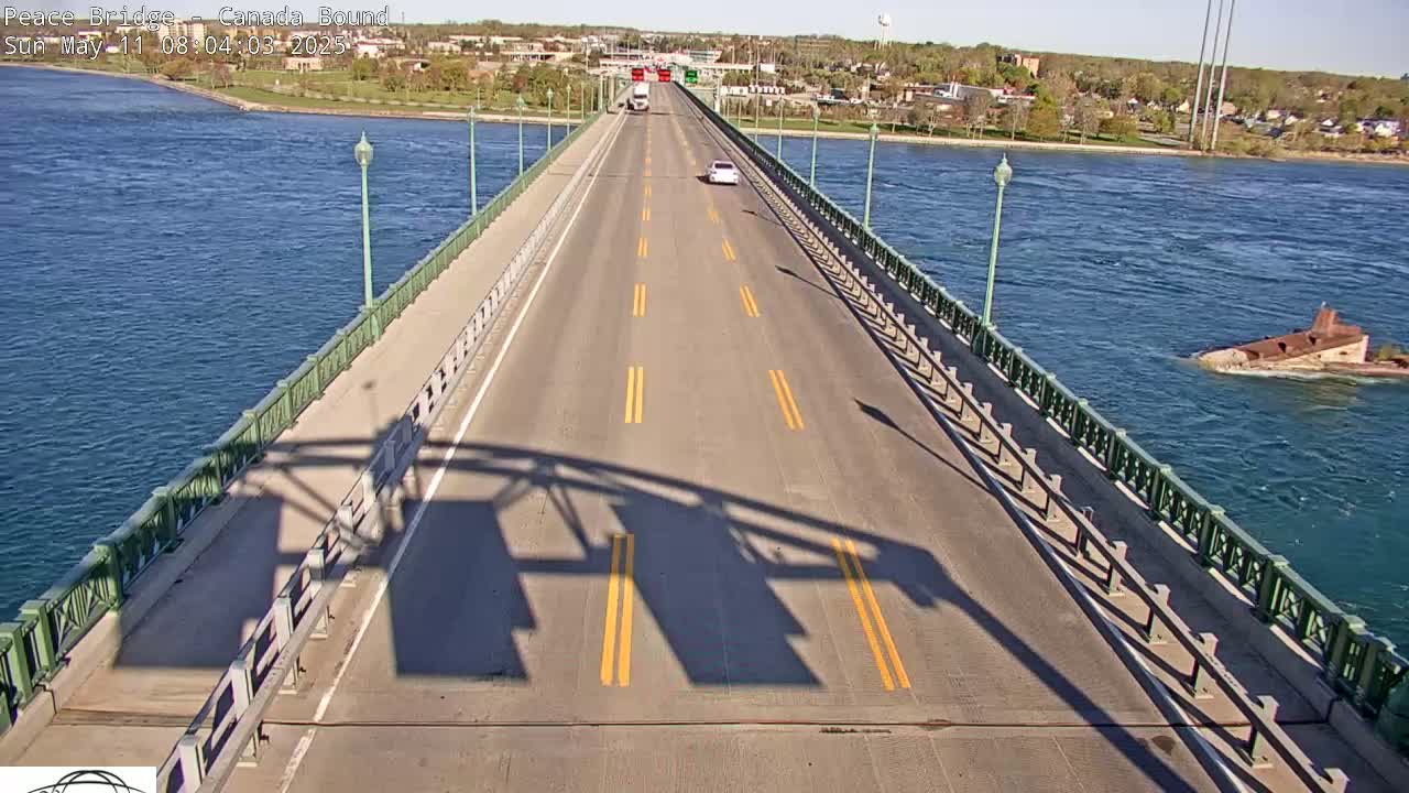 A bridge with a few cars driving on it stretches across a body of water on a sunny day, with a partially submerged structure visible in the water to the right.