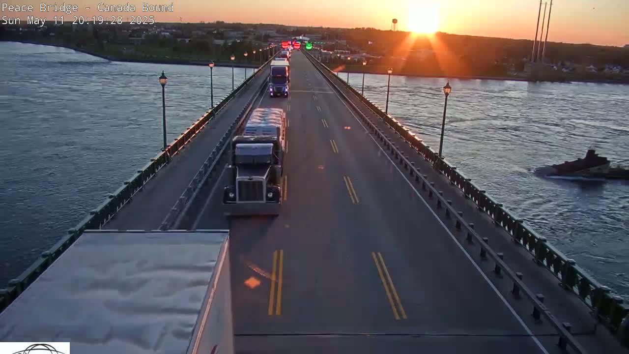 Several semi-trucks are driving across a bridge over a river at sunset.