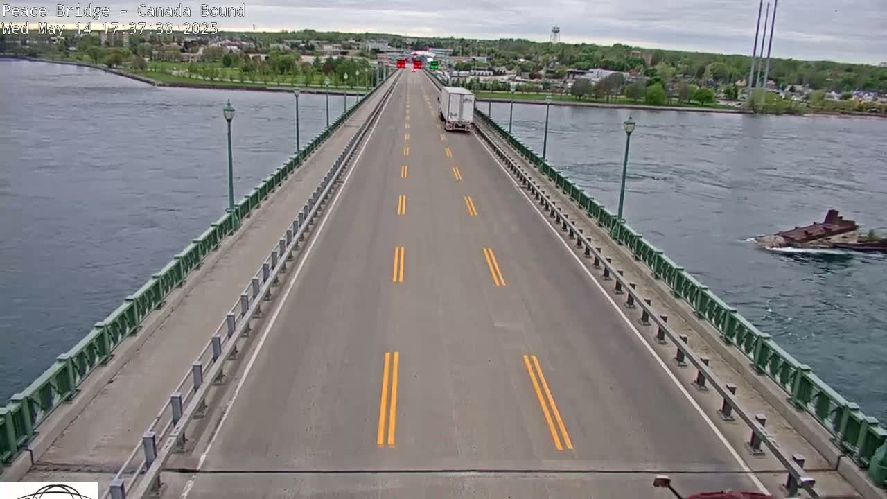A long bridge over water with a single semi-truck driving on it under an overcast sky.