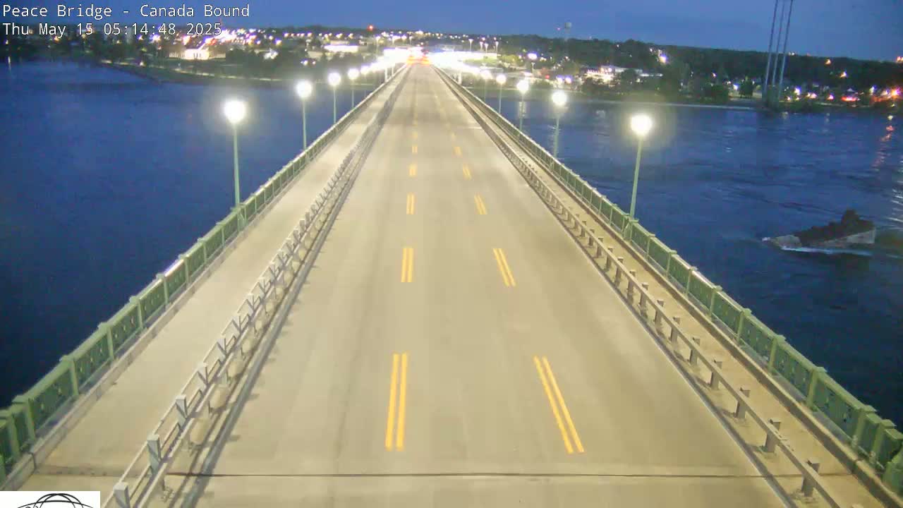 A long, empty roadway on a bridge at night, lit by streetlights, overlooks dark water.