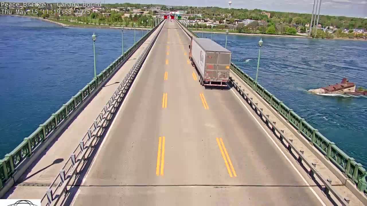 A semi-truck drives across a bridge over a body of blue water on a sunny day.