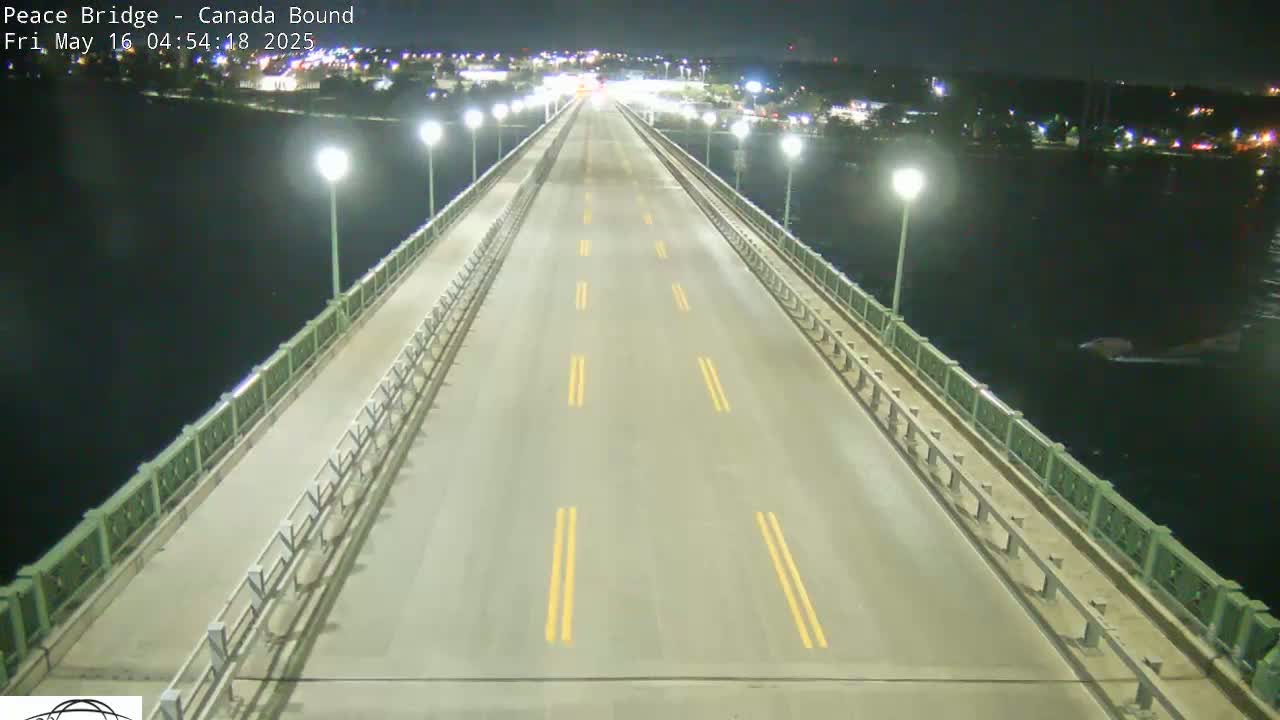 A nighttime view of a sparsely trafficked bridge over dark water, illuminated by streetlights.