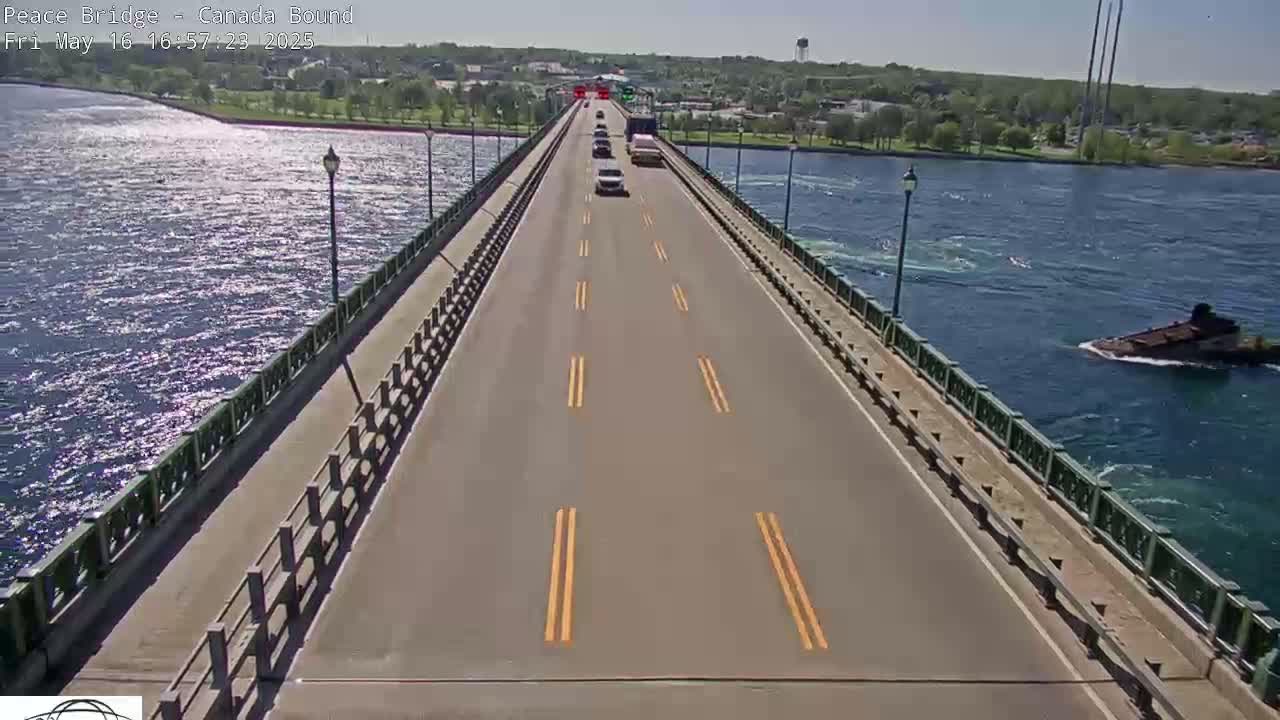 A bridge with several cars driving on it stretches across a body of water under a sunny sky.