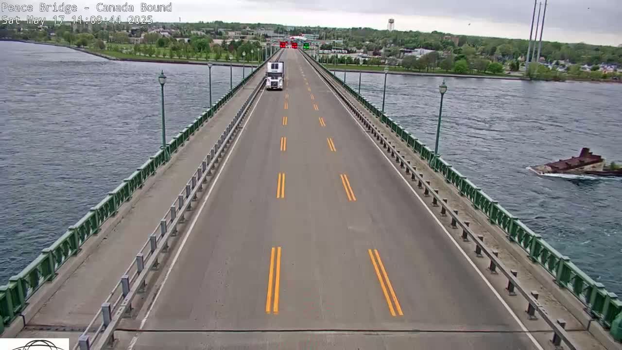 A white semi-truck drives across a bridge over a body of water on an overcast day.