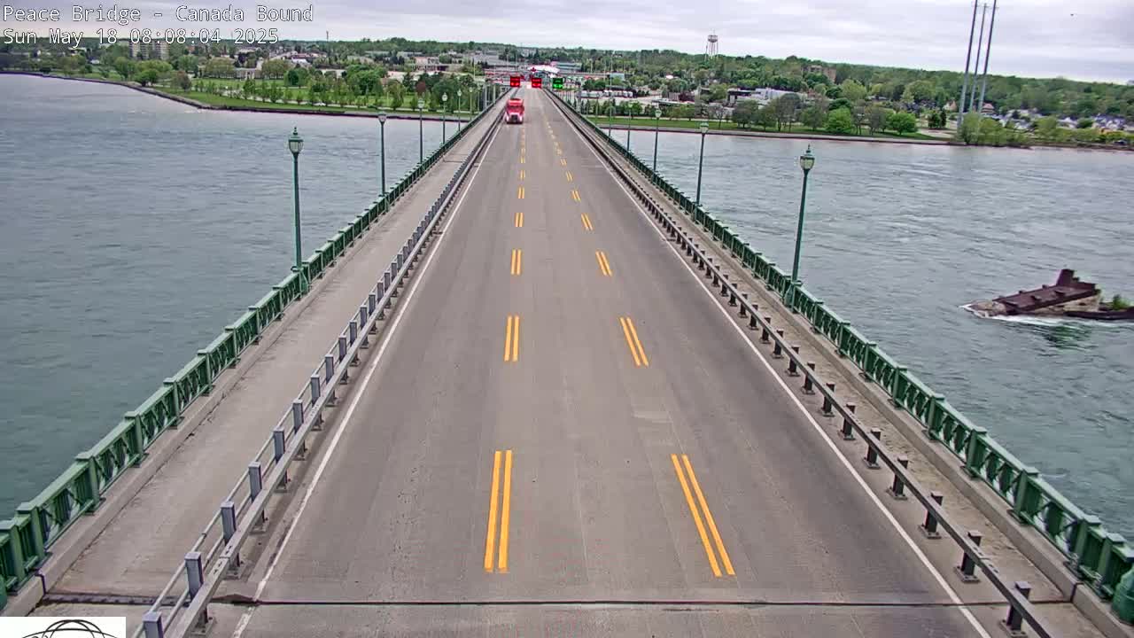 A long bridge with a single lane of traffic in each direction stretches across a body of water under an overcast sky; a sunken vessel is visible in the water to the right.