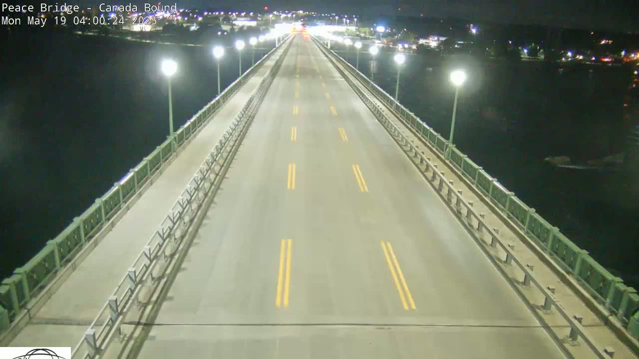 A mostly empty roadway on a bridge at night, lit by lamps, stretches over dark water.