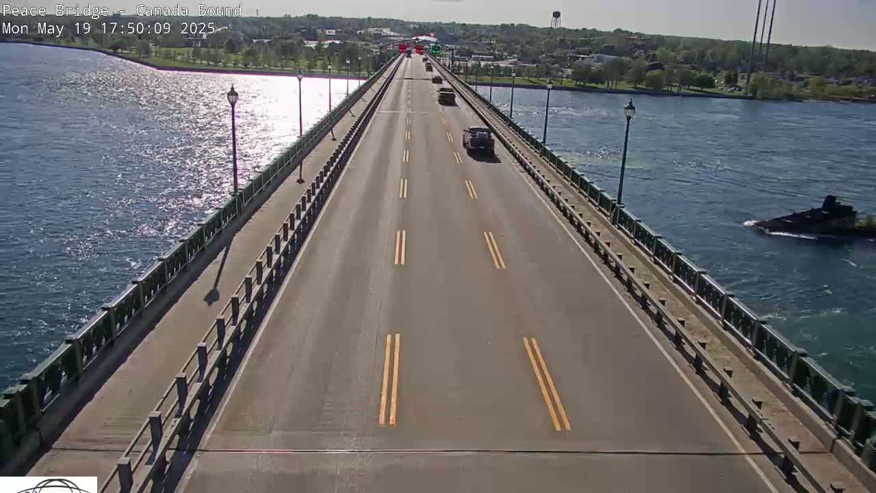 A multi-lane bridge spans a body of water on a sunny day, with several vehicles traveling across it and a dark-colored vessel visible in the water below.