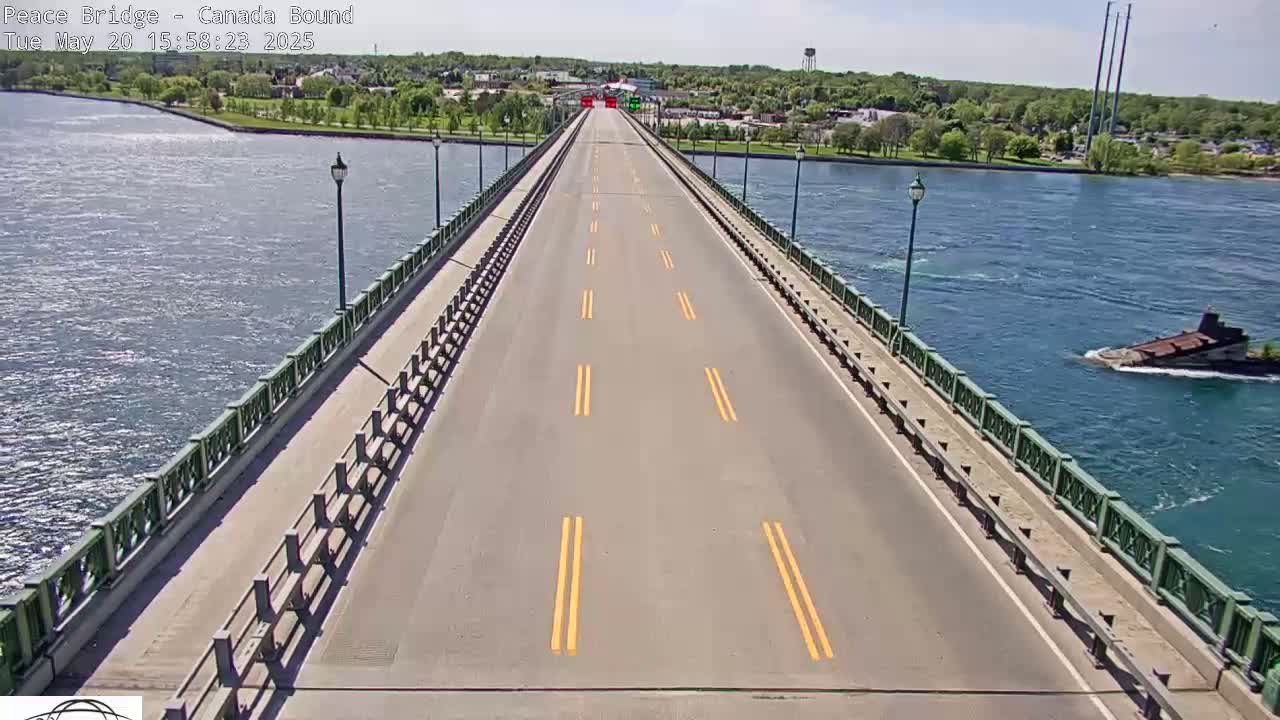 A long, empty road stretches across a bridge over blue water on a sunny day, with green railings and land visible on either side.