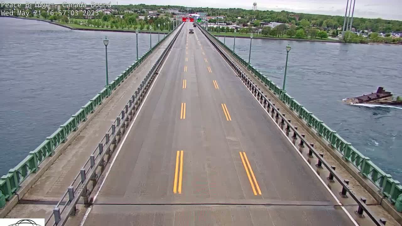 A bridge over water with a few cars driving on it, under an overcast sky.