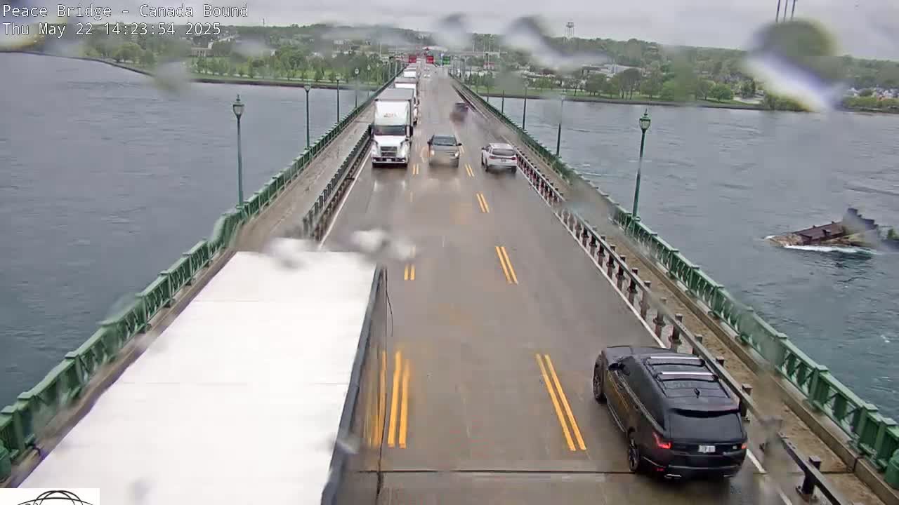 A wet road on a bridge over water with several vehicles driving in both directions under a rainy sky.