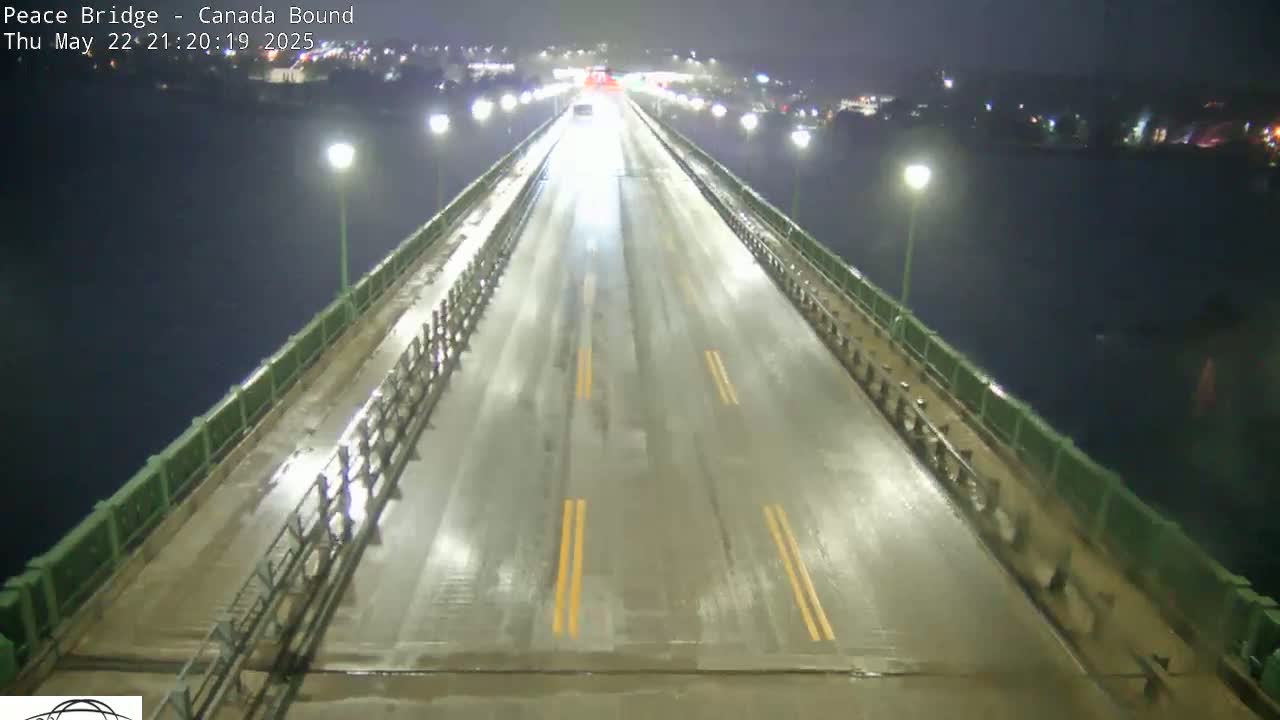 A wet, nighttime view of a bridge roadway with sparse traffic and dark water visible below.