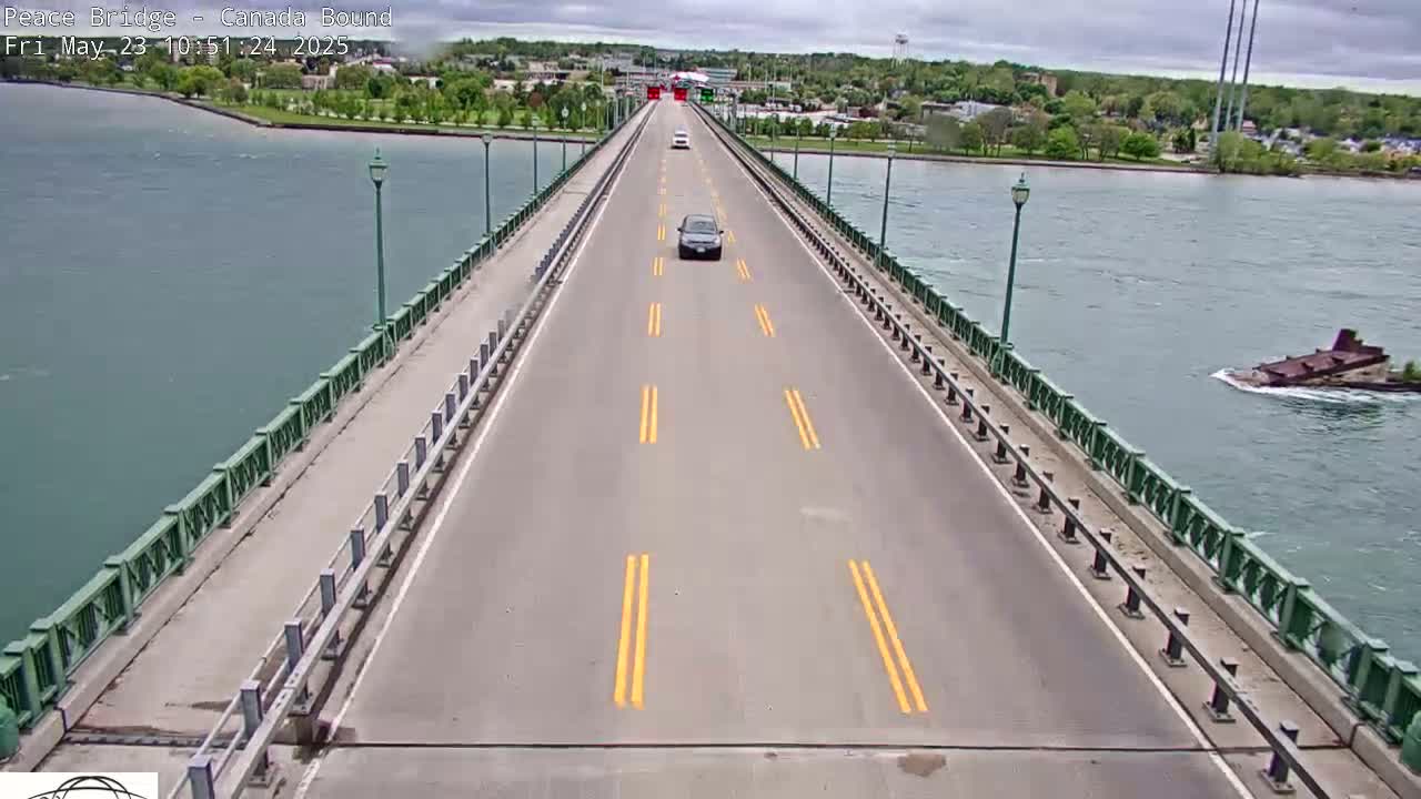 A two-lane bridge stretches across a body of water under overcast skies, with a few vehicles traveling on it and a partially submerged vessel visible in the water.