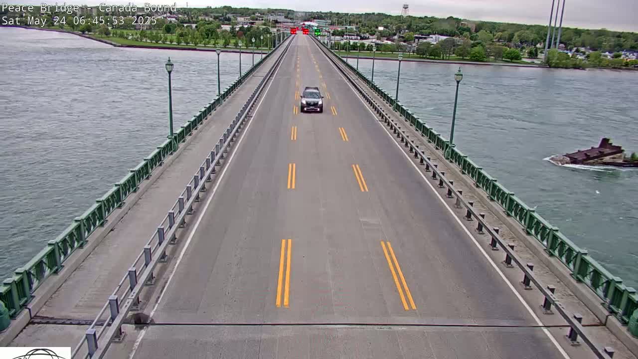 A single vehicle drives across a bridge over a body of water on an overcast day.