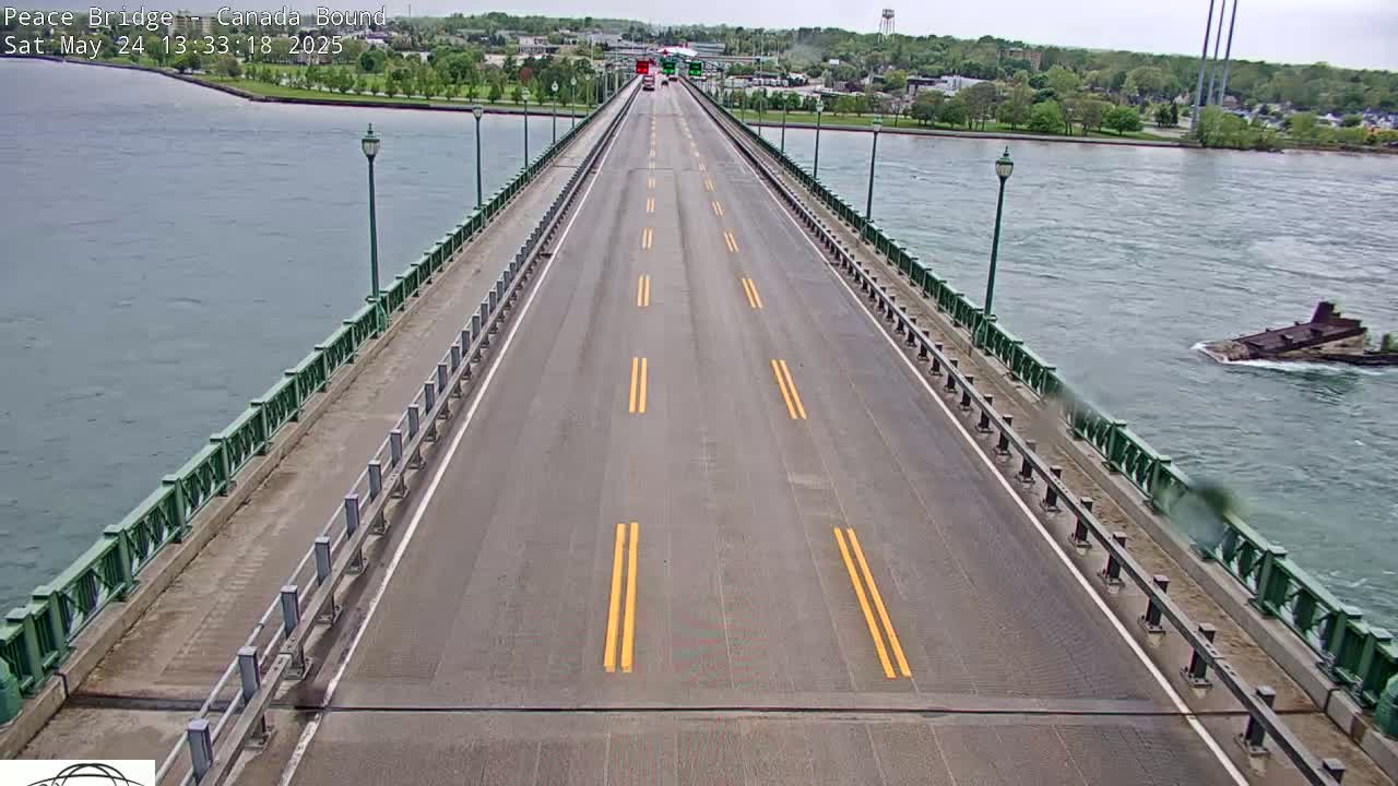 A bridge roadway with light traffic extends over water under partly cloudy skies.