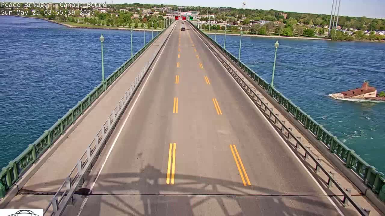 A long bridge over blue water on a sunny day has one car driving toward the viewer.
