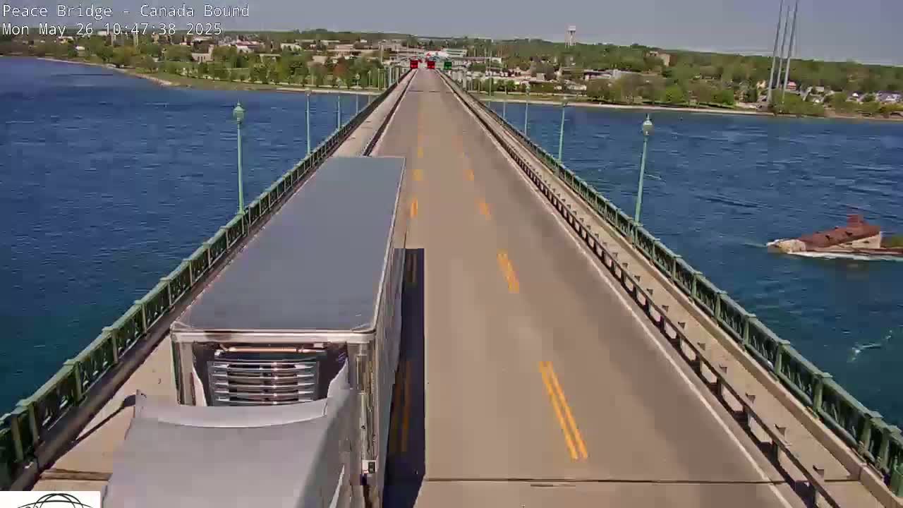A semi-truck drives across a bridge over blue water on a sunny day.