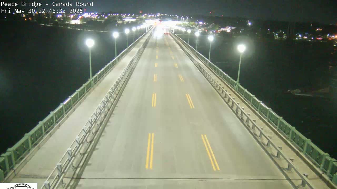A nearly empty highway on a bridge at night, lit by streetlights, overlooks dark water.