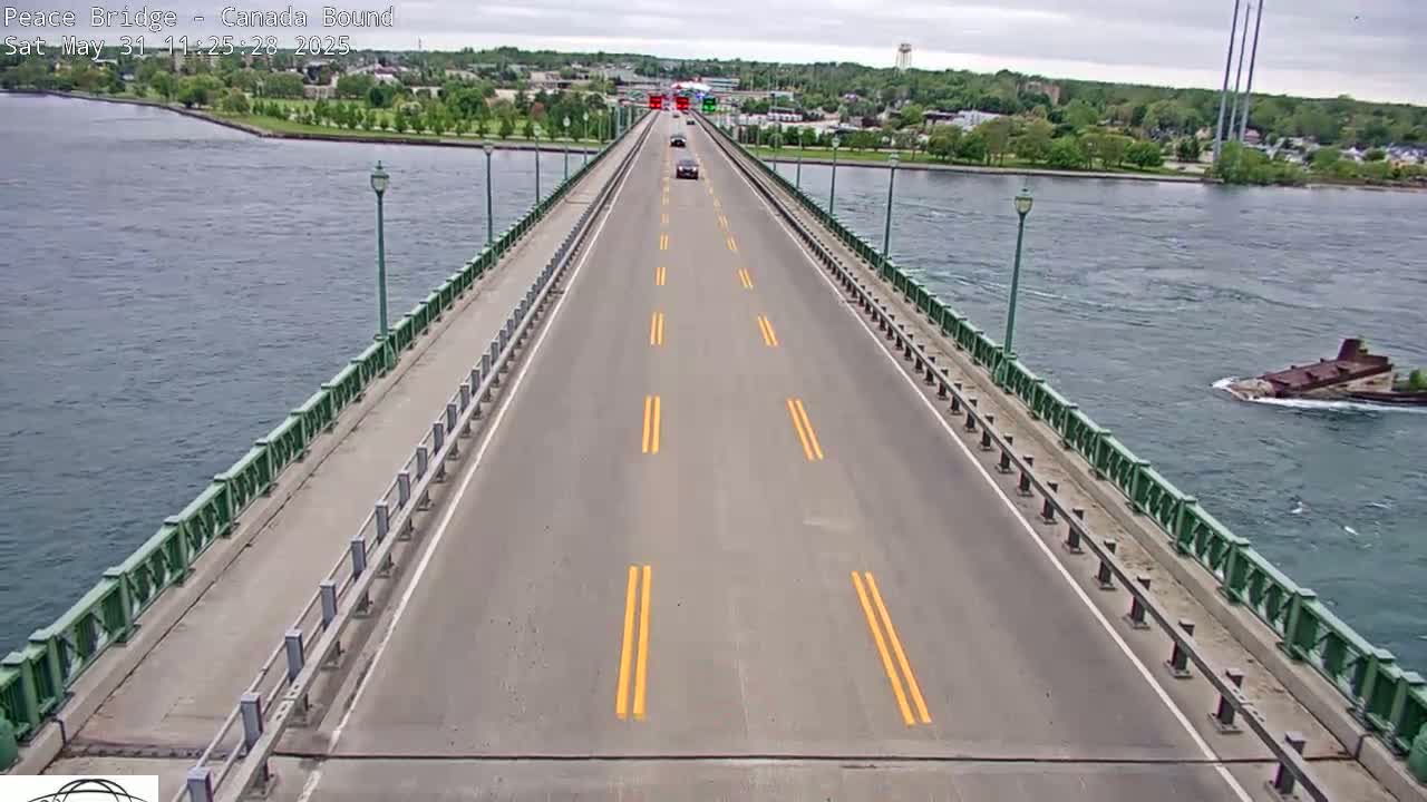 A two-lane bridge spans a body of water under an overcast sky, with a few vehicles traveling on the bridge and a sunken vessel visible in the water.