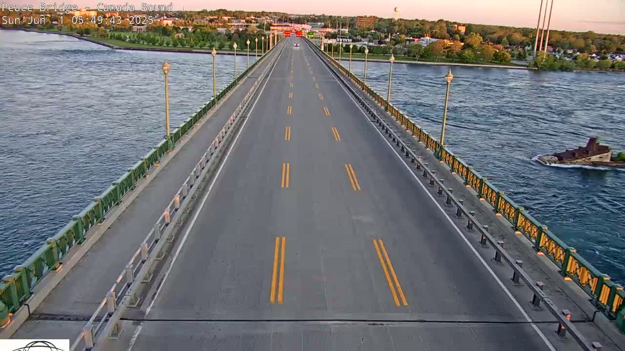 A multi-lane highway crosses a bridge over a river under a partly cloudy evening sky, with a few vehicles visible on the road and a barge in the water.