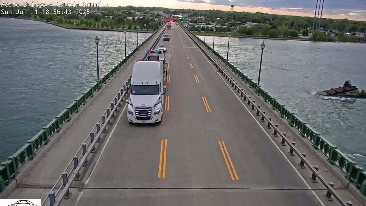 A long bridge over water with a few vehicles driving on it under partly cloudy skies.