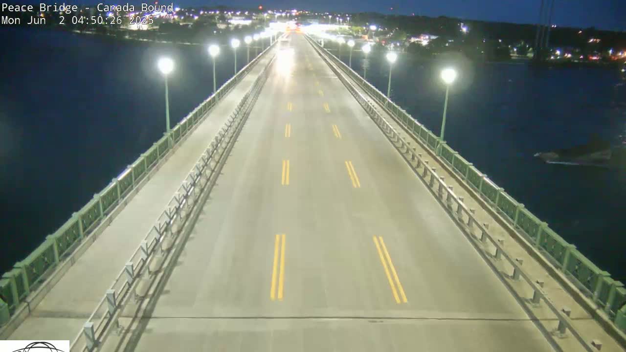 A mostly empty bridge at night, lit by streetlights, stretches over dark water.