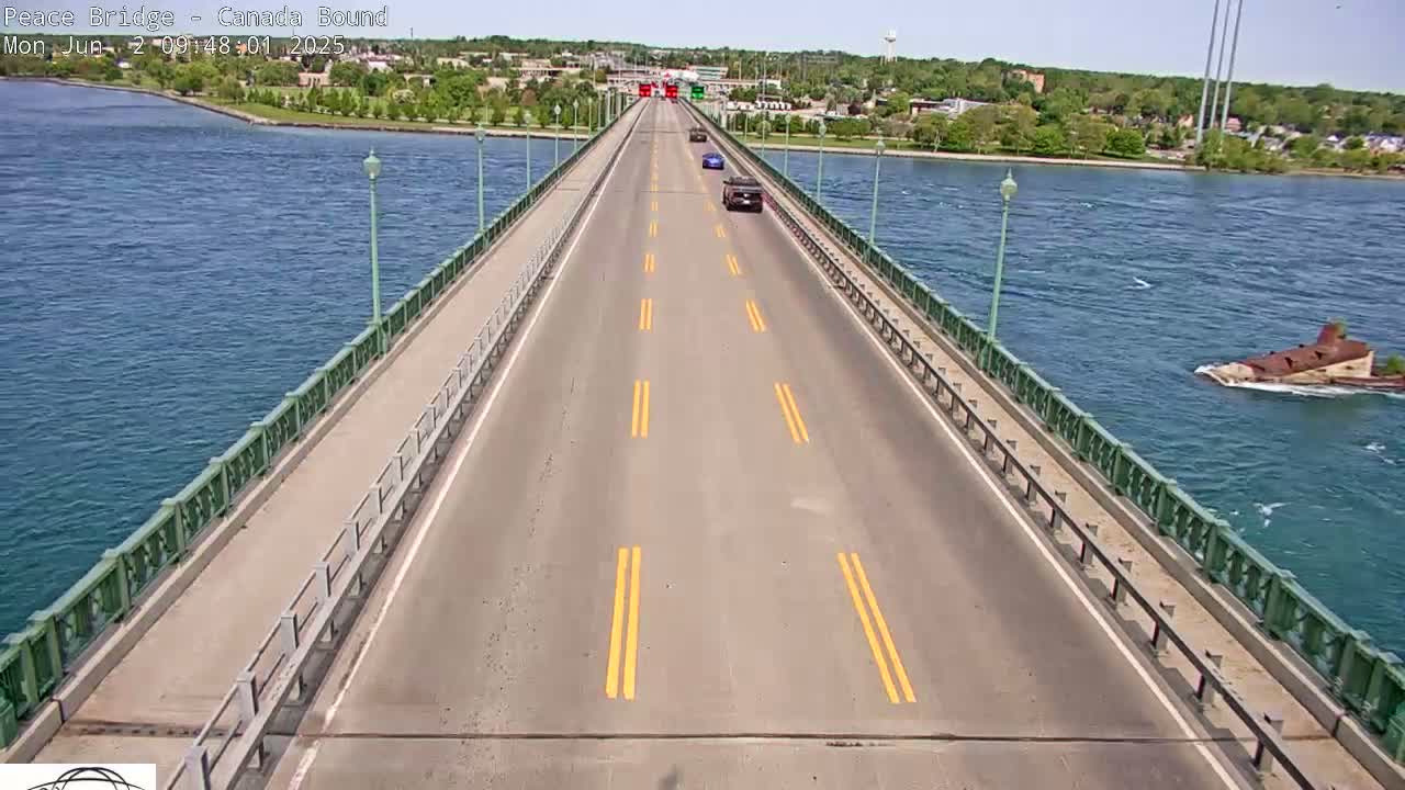 A bridge with a few cars driving on it stretches across a body of water on a sunny day, with a partially submerged structure visible in the water to the right.