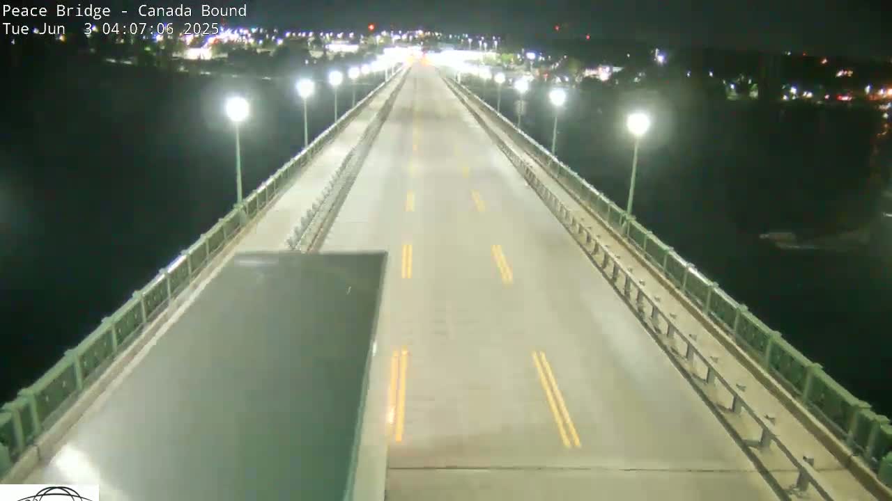 A nighttime, overhead view shows a mostly empty bridge roadway over dark water, lit by streetlights on either side of the road.