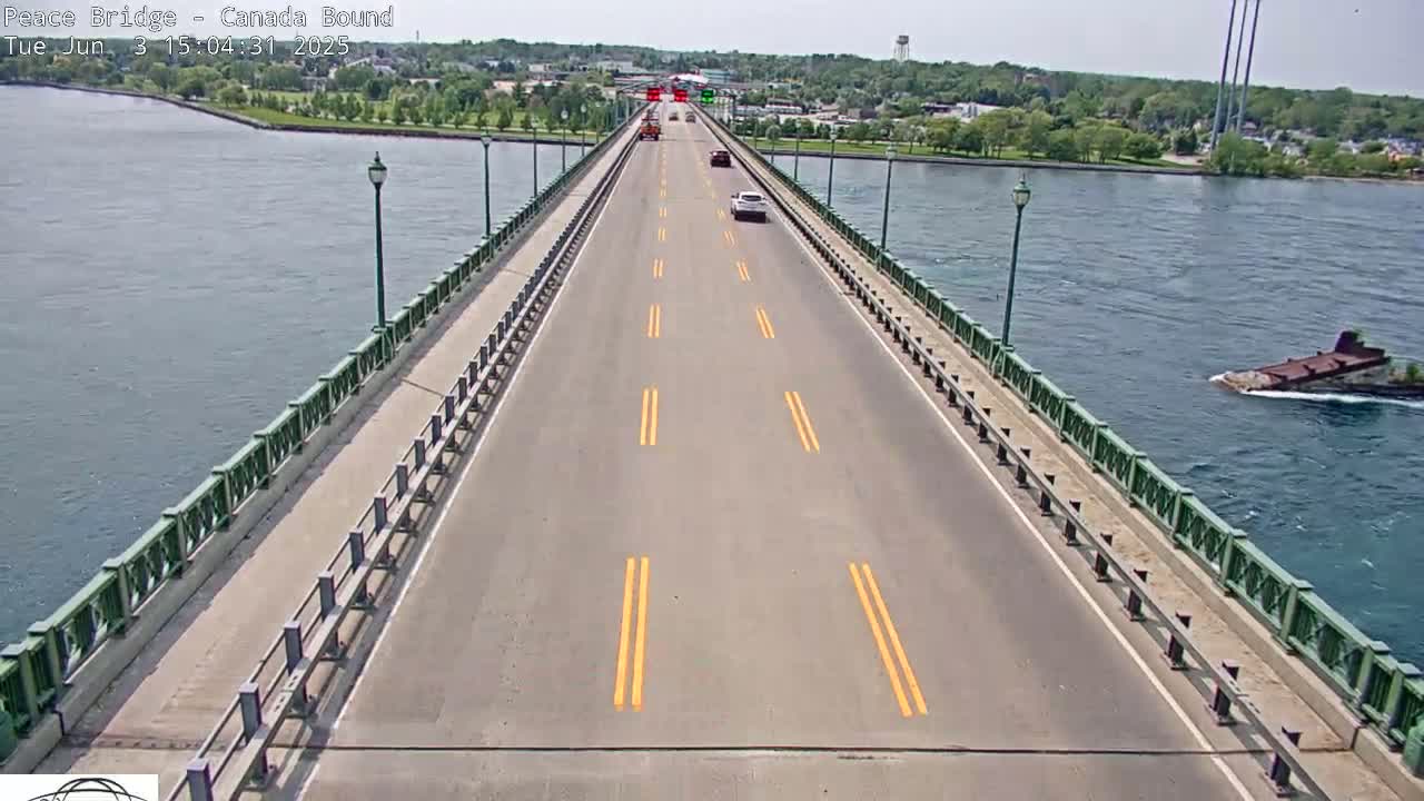 A bridge road with a few cars driving on a sunny day, with water on either side.