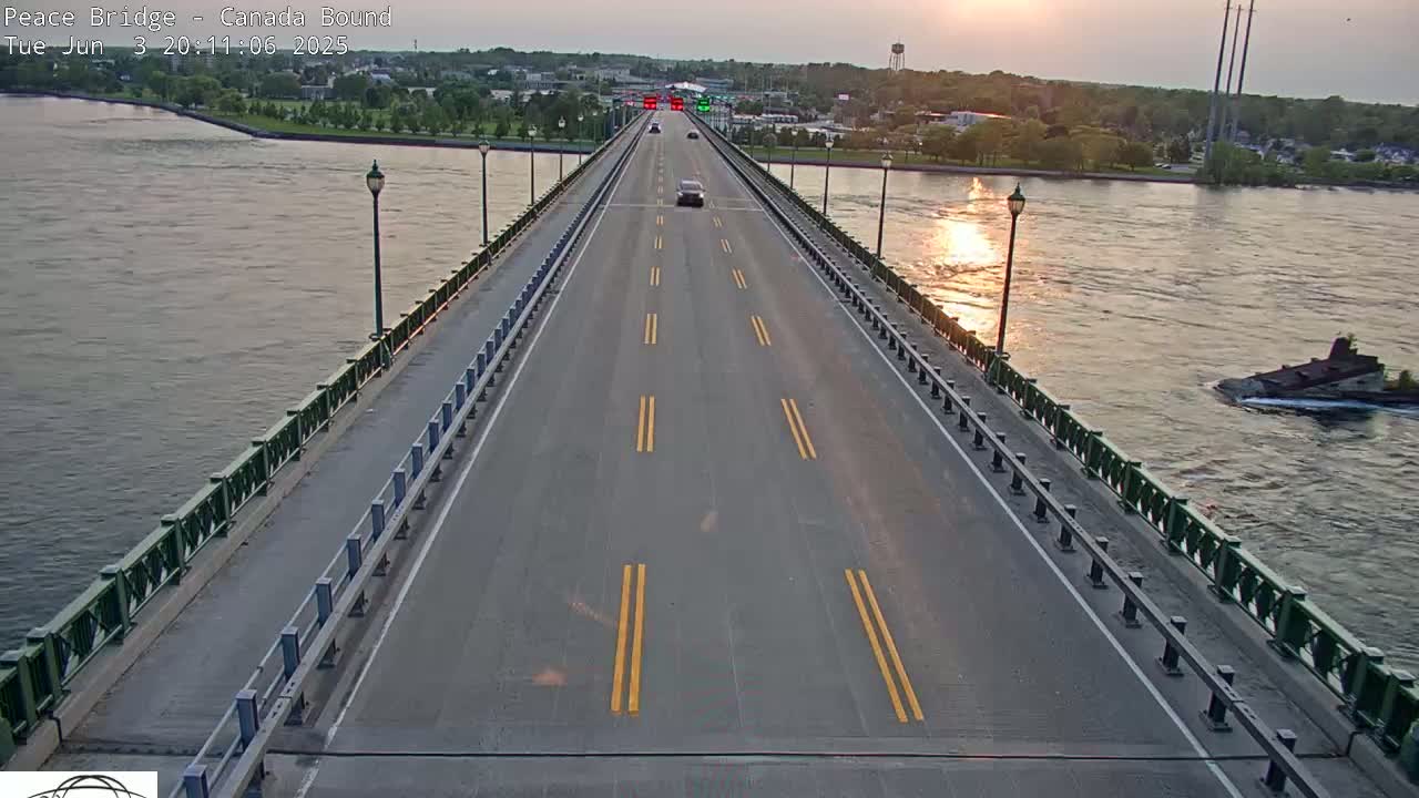 A bridge roadway with few cars, under a setting sun, over a body of water with a small island visible in the distance.