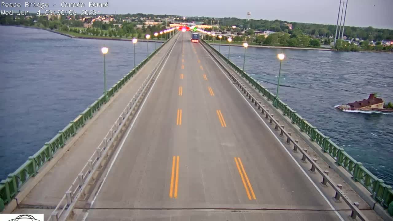 A long bridge over water with a few vehicles on it, under a partly cloudy sky.