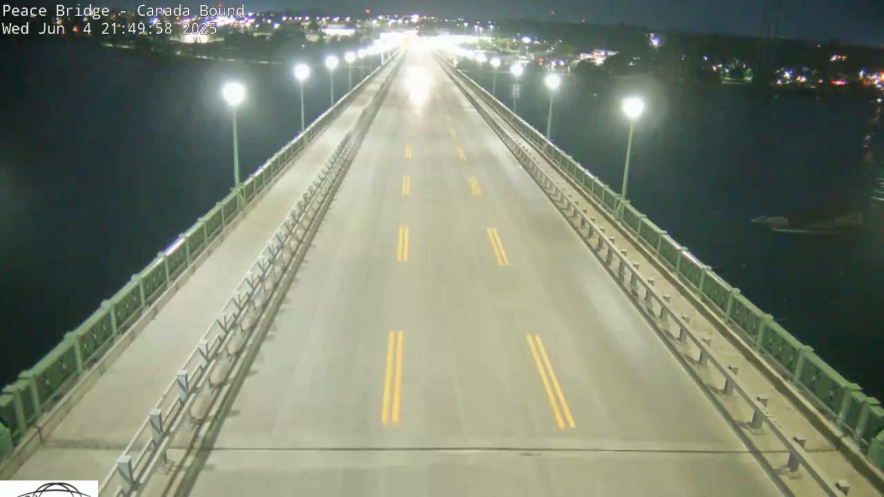 A mostly empty bridge at night, lit by streetlights, overlooks dark water.