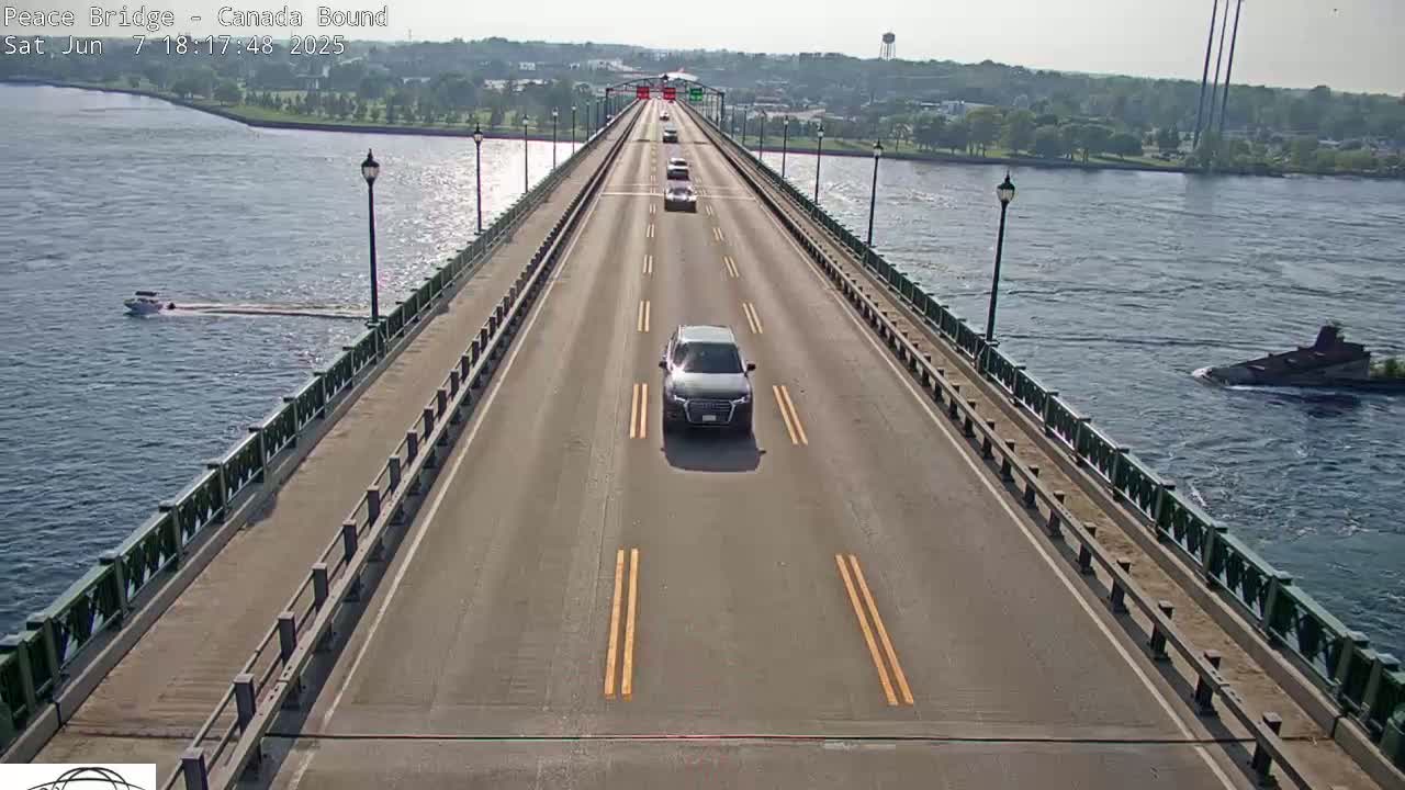 A bridge with several cars driving on it, overlooking a river with a boat and a barge on a sunny day.
