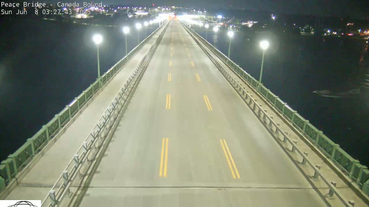 A mostly empty bridge at night, lit by streetlights, spans a dark body of water.