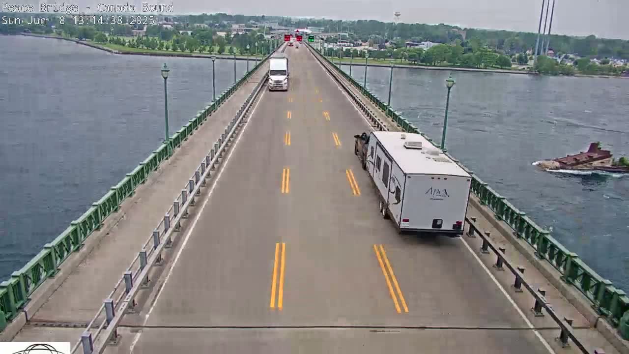 A high-angle view shows a two-lane bridge spanning a body of water on a partly sunny day, with a few vehicles traveling across the bridge and a small island visible in the distance.