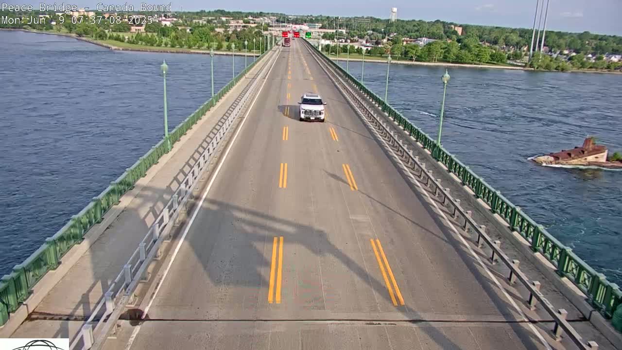 A bridge over water on a sunny day, with a few vehicles driving on the road and a partially submerged wreck visible in the water.