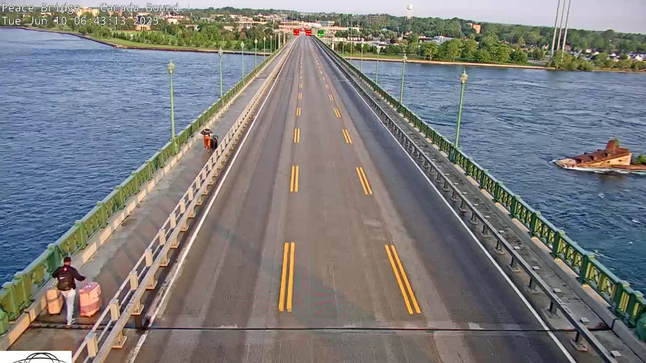 A long bridge over a body of water on a mostly sunny day, with two people walking on a sidewalk next to the roadway.