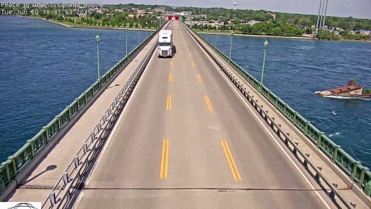 A white semi-truck drives across a bridge on a sunny day over blue water.